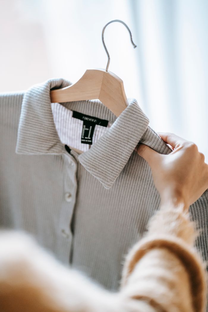 Home Crop anonymous female designer holding wooden hanger with elegant shirt while preparing for fashion event
