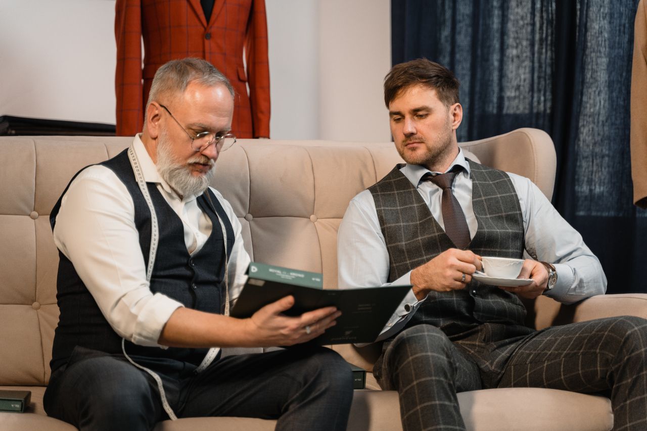 Home Tailor and client reviewing fabric samples for a custom suit in a stylish workshop.
